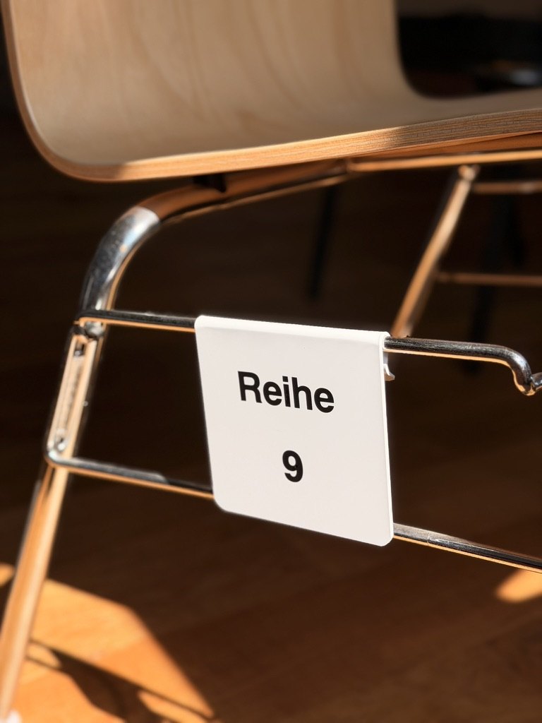 Weißes Reihenschild Reihe 9 montiert am Stuhlgestänge