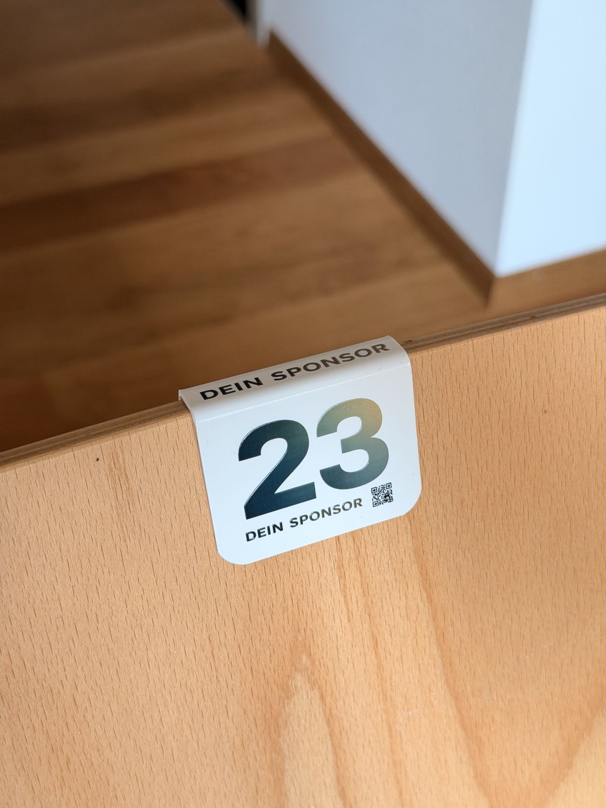 UV-Vollfarbdruck: Stuhlnummer mit Sponsorenlogo und QR-Code auf Holzlehne